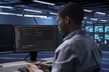 Yazılım geliştiricisi sunucu çiftliğini müşterilerin veri işleme gereksinimleri için optimize ediyor. Veri merkezi ekipmanlarını verimli bir şekilde çalıştıran Afrikalı Amerikalı bir adam