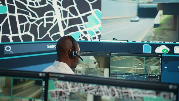 stock image Operator uses satellite navigation map to guide delivery truck drivers, works in observation room to avoid traffic. African american employee tracing orders within the surveillance system. Camera B.