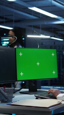Veri merkezindeki dikey video mühendisi bilgisayar kullanarak güvenlik tehditlerini izliyor, siber güvenlik önlemleri uyguluyor. Yeşil ekran PC kullanan adam, yönetmeliklere uyulmasını sağlıyor, kamera B