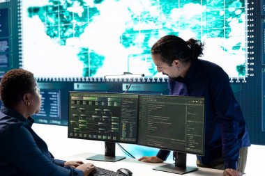 Bir grup hükümet korsanı bir ağı ele geçirmek için hackleme araçları kullanıyor, siber savunma ve veri koruma önlemlerine odaklanıyor. Uzman ekip büyük ekranda önemli bilgileri inceliyor.