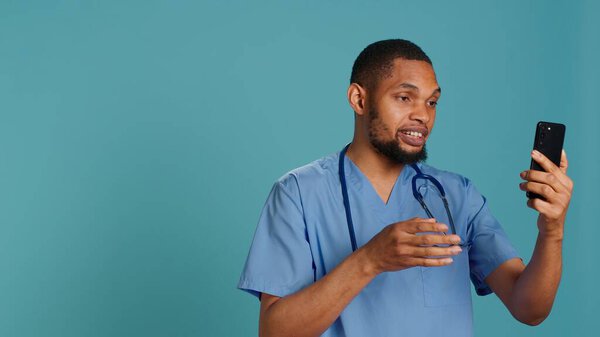 Мужчина медбрат на видеовстрече с помощью мобильного телефона, здоровается с людьми. Специалист по здравоохранению в области телемедицины онлайн с пациентами на смартфоне, изолированный на фоне студии, камера А