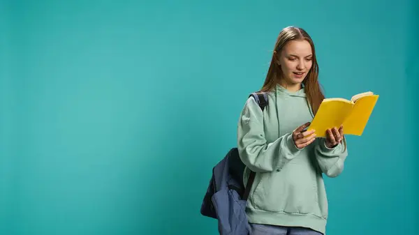 stock image Teenage woman with book in hands showing appreciation for literature, isolated over studio background. Young reading enthusiast holding novel, enjoying reading hobby, camera B