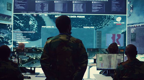 Сержант следит за спутниковыми снимками на большом экране, собирает информацию для будущих военных операций. Армейский офицер использует разведывательную систему в командном пункте. Камера B.