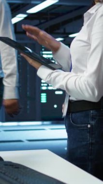 Dikey Veri Merkezi bilgisayar bilimcisi, optimum performans ve güvenilirliği sağlamak için altyapıyı tasarlıyor, uyguluyor ve yönetiyor. Sunucu odasındaki kadın tablet üzerinde kodlama yapıyor, kamera B