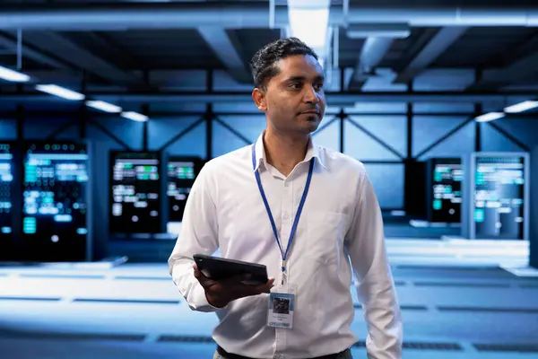 Stock image Admin in server hub checking recovery plan on tablet, monitoring data center energy consumption across components, making sure sensors are functioning optimally, doing routine disk checks