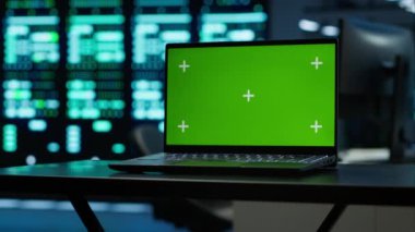 Yüksek teknoloji veri merkezindeki mühendislerin güvenlik tehditlerini izlemek için kullandıkları yeşil ekran laptopuna odaklan. Yönetmeliklere ve kamera A 'ya uyum sağlayan işçilerin kullandığı model defteri kapat.