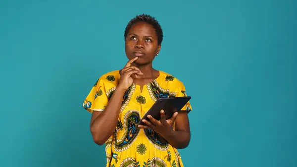 stock image Young woman checking her social media platforms in studio, browsing internet network webpages against blue background. Natural sweet girl posing with tribal native traditional clothing. Camera A.