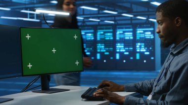 Afro-Amerikan yazılım geliştirici yeşil ekran bilgisayarda kodlama, güncelleme ekipmanları. Renkli anahtar monitörü kullanarak sunucu kümelerini denetleyen bir sistem yöneticisi