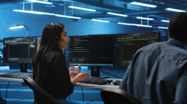 Bilgi işlem destek uzmanlarından oluşan bir ekip bilgisayar ağı güvenlik veri merkezinde sunucu sıralarını denetliyor. Meslektaşlarının yanında mikrofonla konuşan ve süper bilgisayarları denetleyen bir kadın.