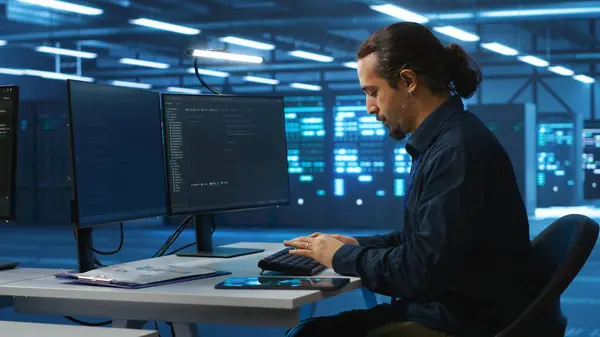 stock image System administrator in server room doing system analysis, coding, doing needed adjustments for supercomputers to run. Specialist working in high tech facility housing advanced storage infrastructure