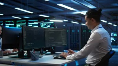 Veri merkezinde sunucuları, işletim sistemlerini ve yazılım programlarını yöneten iyimser yöneticinin portresi. Sunucu merkezinin güvenli ve düzgün çalıştığından emin olmak için neşeli bir uzman, kamera B