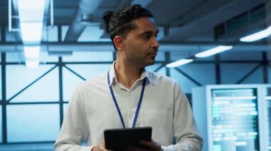 Altyapı enerji tüketimini yönetmek için kullanılan yüksek teknoloji veri merkezinde yürüyen programcı tablet üzerinde çalışıyor. Sunucu çiftliğinde otomasyon için kullanılan çalışma alanındaki Hintli adam, kamera A