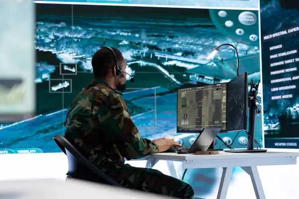 stock image Military personnel in a modern command center work on data processing, integrating real time surveillance footage from satellite systems. Working with big screen and computer intelligence.