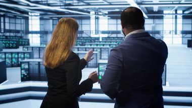 Takım çalışanı yönetici meslektaşlar sunucu odası donanımını inceliyor. Bilgi işlem uzmanı ve iş arkadaşı veri merkezi kurulumunu denetliyor, ekipmanları kontrol ediyor, performansı izliyor, kamera A