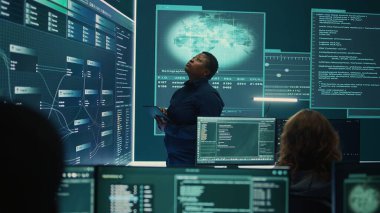 Bir hükümet güvenlik operasyonları merkezinde çalışan profesyonel bilişim uzmanı büyük ekrandaki verileri analiz ediyor. Siber güvenlik izleme ve tehdit analizinin önemini vurgulamak. Kamera B.