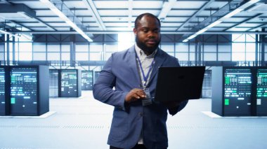 Modern veri merkezinde dizüstü bilgisayar üzerinde çalışan bilişim mühendisi, sunucu işlemleri, sistem bakımı ve siber güvenlik protokolleri, optimal performans ve veri bütünlüğü sağlanması, kamera B