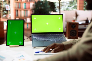 İşadamı dizüstü bilgisayar ve tabletteki izole edilmiş maket ekranlara bakıyor ve başlangıç kârını artırmak için uzaktan çalışma yapıyor. Girişimci, muhasebe verilerini kendi masasında inceliyor..