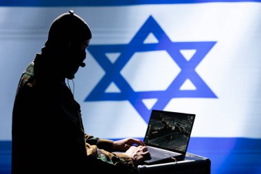 Maskeli Mossad ajanı izleme verilerini analiz etmek için İsrail bayrağının arkasında izole bir şekilde duran bir cihaz kullanıyor. İsrail gizli ajanı uluslararası operasyonda görevini tamamladı