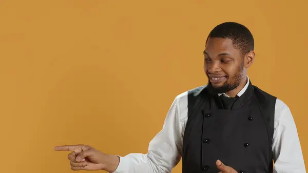 stock image Waiter in professional uniform pointing at something to the left or right, creating a commercial ad for five star service oriented restaurant. Catering staff in hospitality industry. Camera A.