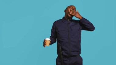 Uyanık kalmak için kahve fincanı içen yorgun güvenlik görevlisi, suçluları önlemekle görevlendirildi. Gece vardiyasında kafeinli içecek yudumlayan yorgun korumaların portresi, stüdyo arka planı, kamera B