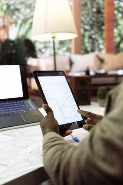 İşyeri sahibi, yeni ofis yeri taşıma planının planlarını ve planlarını analiz ediyor. Yaratıcı bir iş yeri kiralama işine yatırım yapıyor. Ev masasında mimari taslaklar hazırlanıyor.