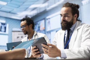 Uzman doktorlar röntgen taramalarını tartışıyor. Teşhis koymadan önce hastane kayıtlarına bakıyorlar. Lisanslı tıp personeli hastalıkların önlenmesi için toplu iş yapıyor..