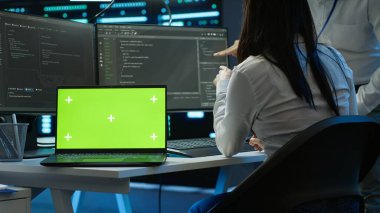 Veri merkezindeki programcı krom anahtar defteri kullanarak veri tabanlarını yönetir ve korur, veri bütünlüğü ve güvenliğini sağlar. İzole edilmiş ekran dizüstü bilgisayar ve kamera A kullanarak sunucu odası sistemlerini güncelleme uzmanı