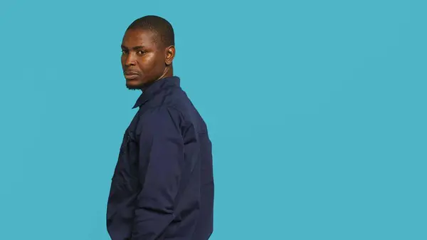 stock image Security guard turning around after hearing suspect sounds during surveillance shift, ensuring protection. Portrait of man in uniform standing isolated with back against studio background, camera A