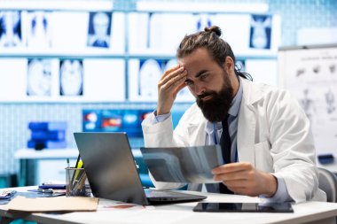 Sinirli hekim röntgen taraması sonuçlarını analiz ediyor ve hastalığı bulmakta zorlanıyor, en iyi tedavi planını uygulamak için baskı altında hissediyor. Doktor özel bir klinikte endişeli ve yorgun.