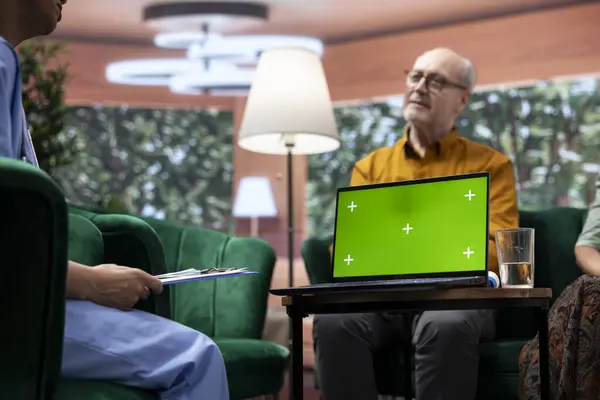 stock image Caregiver nurse consulting senior couple next to chroma key mockup display on laptop, discussing about medical treatment and prescription. Specialist offering support and assistance.