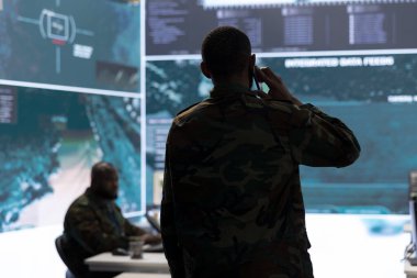 Askeri görevli, potansiyel tehditleri takip etmek ve gerçek zamanlı verileri izlemek için gelişmiş teknoloji ve uydu görüntüleriyle çalışan bir görev kontrol merkezinde telefon görüşmelerine cevap veriyor. İstihbarat faaliyetleri.