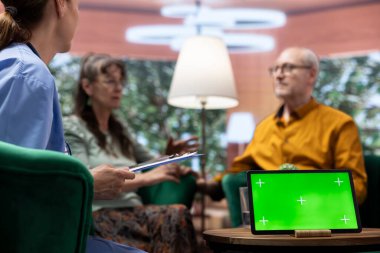 Yaşlı bir adam ve kadın evlerinde yeşil ekranlı bir tabletle hemşirelerle konuşuyor, eğlenceli bir sohbet ediyorlar ve rehberlik istiyorlar. Yaşlı çift iyi hissediyor, check-up ziyareti sırasında dinleniyorlar..