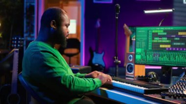 Erkek sanatçı ev stüdyosunda elektronik piyano klavyesinde müzik yapıyor. Ses mühendisi, akustik aletler ve teçhizatla MIDI kumandasını oynuyor, kayıt yapıyor ve bir film müziği besteliyor. Kamera A.