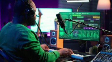 Genç sanatçı piyano tuşları çalıyor ve mikrofonda şarkı söylüyor, yeni müziğini besteliyor ve dijital arayüzde şarkıları karıştırıyor. Yapımcı teknisyen teçhizatlı bir melodi besteledi. Kamera A.