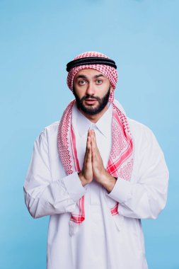 Geleneksel giysiler içinde yüzen plakalarla dua eden, Tanrı 'dan af dileyen ve kutsanmış portre için dua eden Müslüman bir insan. Dini bütün Arap adam başörtüsü takıyor, yalvarıyor ve kameraya bakıyor.