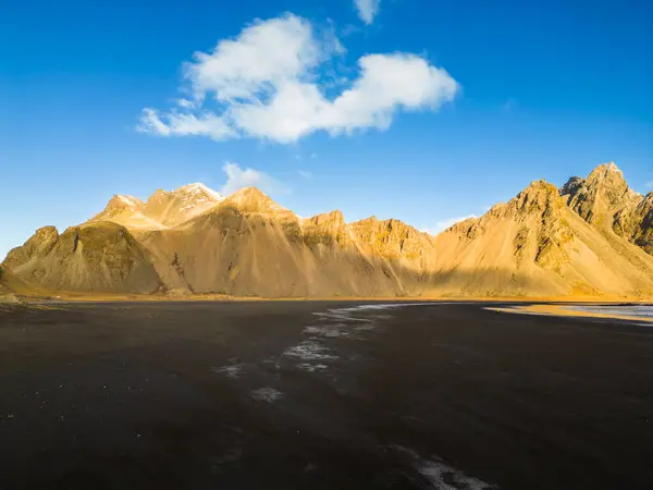 stock image Black sand beach with huge rocky hills in amazing nordic surroundings, famous vestrahorn mountains and fields in Iceland. Stokksnes beach creating wintry landscape, arctic ocean shoreline.