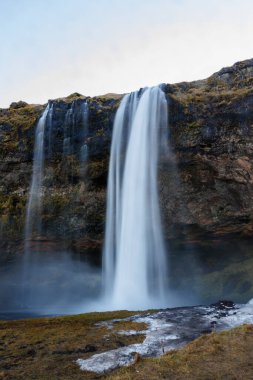 Kayalıklardan aşağı akan İzlanda çağlayanlarından akan nehir akıntısı, karlı donmuş dağ veya tepeden akan su akıntısı. İzlanda 'da nefes kesici doğal seljalandfoss şelalesi, vahşi kutup manzarası.