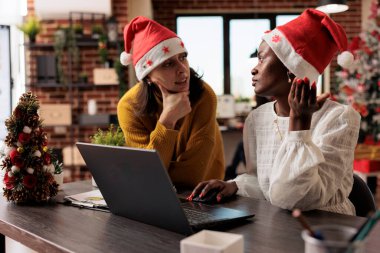 Çalışan kadınlar, Xmas 'ın süslü ofisinde dizüstü bilgisayarla çalışırken başlangıç planını tartışıyorlar. Afrika kökenli Amerikalı ve Kafkasyalı meslektaşlar yeni yıl şenlikli işyerinde konuşuyorlar