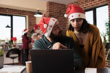 Yılbaşı mevsiminde ofiste çalışırken dizüstü bilgisayardaki iş arkadaşları tartışır ve çözer. Noel Baba şapkalı beyaz erkek ve kadın iş arkadaşları bilgisayar raporlarını kontrol ediyorlar.