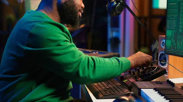 stock image Skilled male composer producing new songs on his mixing console, operating on professional gear in home studio. Artist audio engineer twisting knobs to adjust sound levels on tracks. Camera A.