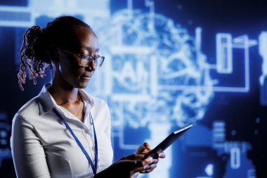 Afro-Amerikan yönetici, yapay zeka sinirsel ağlarını görüntülemek için arttırılmış gerçekliği kullanarak tablet üzerine kod yazıyor. Yüksek teknoloji çalışma alanı denetleyicisi bilgi işleme için yapay zeka betiği çalıştırır