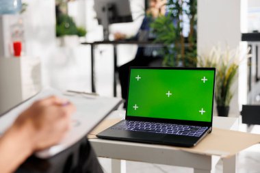 İş sunumu için eş çalışma alanında krom tuşlu yeşil ekranlı dizüstü bilgisayar. Modern yeşil açık uzay ofisinde boş ekranı olan kurumsal taşınabilir bilgisayar