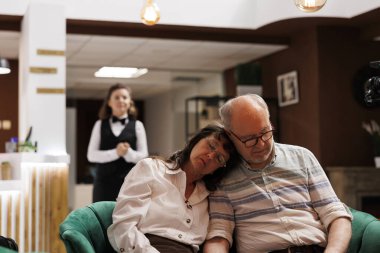 Kafkasyalı yaşlı çiftin rahat koltukta dinlendiği rahat bir otel lobisi. Fotoğrafta, emekli yaşlı bir adam ve bir kadın modern dinlenme odasındaki kanepede uyuyor ve kayıt için bekliyor..