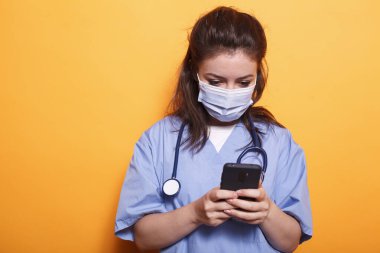 Beyaz kadın doktor, Coronavirus 'a karşı maske takarken modern teknolojiden faydalanıyor. Salgın sırasında cep telefonuna steteskop mesajı atan tıbbi asistanı..