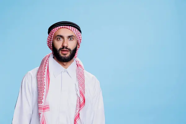 stock image Surprised muslim man dressed in traditional clothes looking at camera with wide eyes. Arab person wearing islamic checkered headscarf and thobe while posing with shocked expression portrait