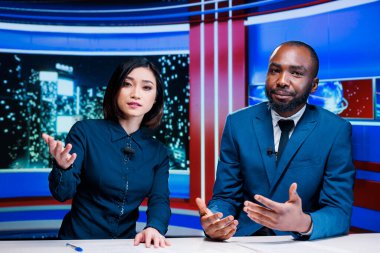 Night show hosts reviewing breaking news live on television program broadcast, working together to create interesting content for tv channel. Diverse team of journalists in newsroom.