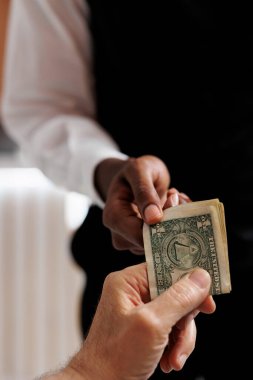 Close-up shot of tourist giving cash tip to african american concierge for helping with luggage in hotel reception. Elderly guest tipping bellboy in luxury lounge area. Photo focus on cash tip. clipart