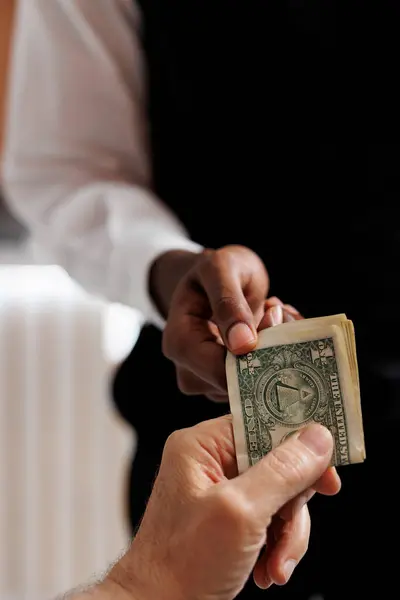 stock image Close-up shot of tourist giving cash tip to african american concierge for helping with luggage in hotel reception. Elderly guest tipping bellboy in luxury lounge area. Photo focus on cash tip.