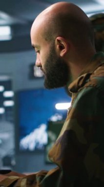 Askeri üste görev yapan dikey görüntülü asker dijital radar ekipmanlarıyla gözetleme yapıyor, füze sistemleri çalıştırıyor. Ortadoğulu bir adam, yetkisiz kişiler için ordu merkezinin güvenlik kameralarını izliyor.
