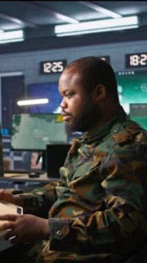 Görev Kontrol Merkezi 'ndeki dikey video askeri ulusal güvenlik operasyonlarını denetliyor, klasör dosyalarını okuyor. Afro-Amerikan ordu uzmanı izleme odasındaki verileri kontrol ediyor.